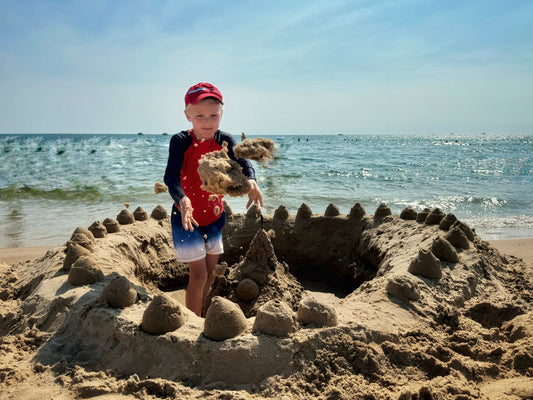 boy making sand castle on the beach by the water wearing sustainable eco-friendly rashguard by primary