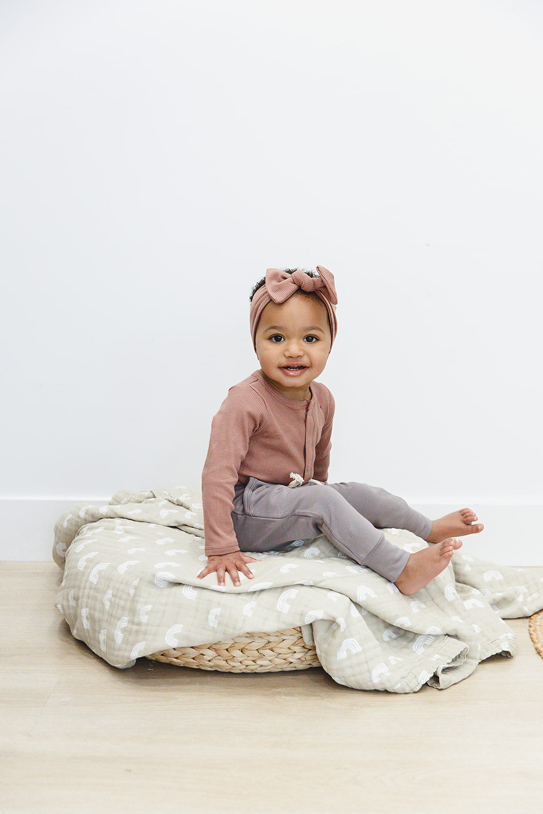 baby girl sitting smiling wearing organic cotton mebie baby rusty rose long sleeve bodysuit onesie and matching bow head band