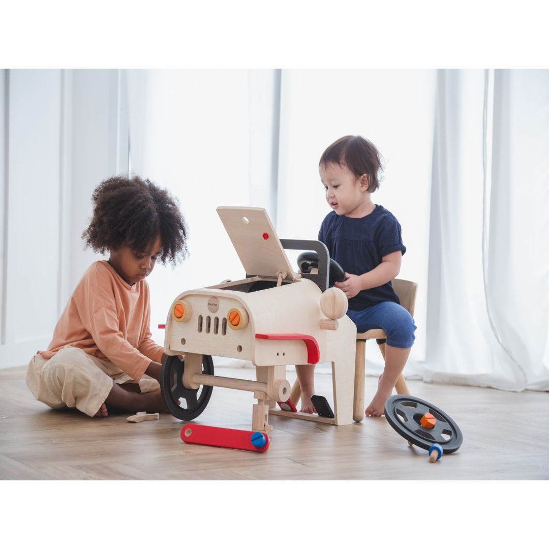 two little kids playing pretend mechanic with eco-friendly wooden mechanic car toy by plantoys