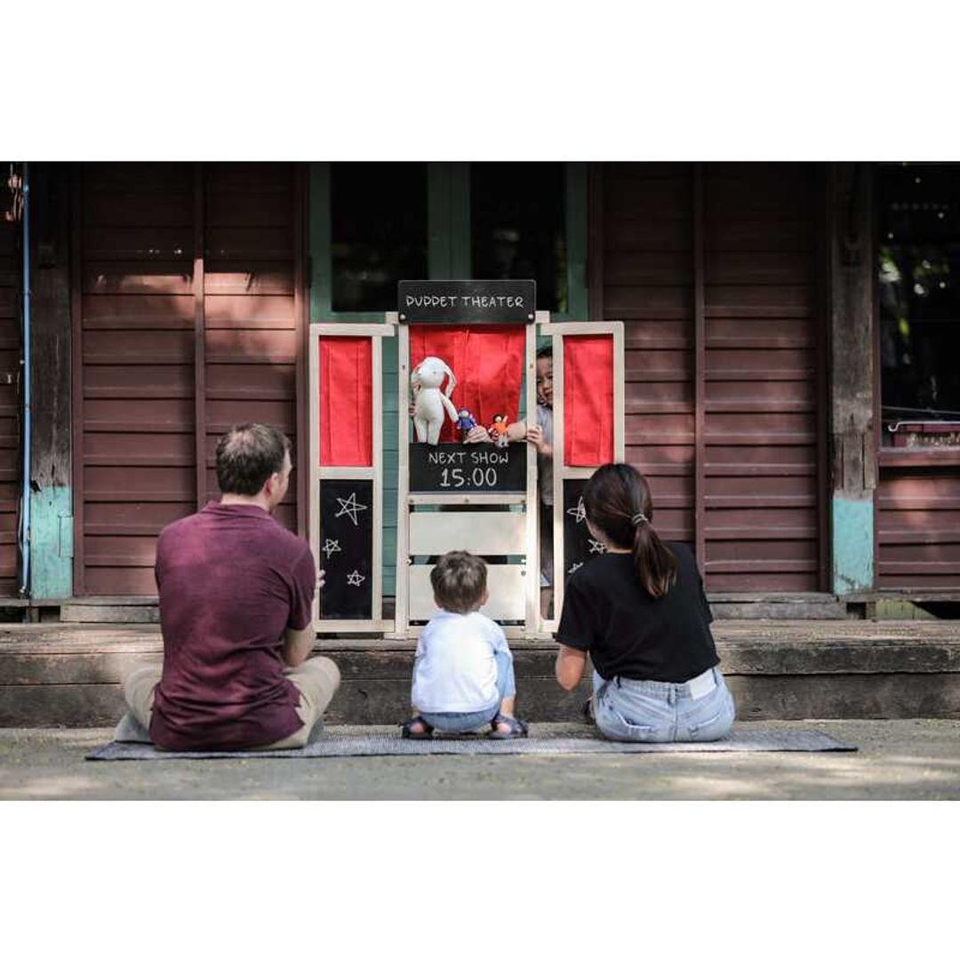 family watching puppet theater performance by a little boy playing eco-friendly wooden play center by plantoys