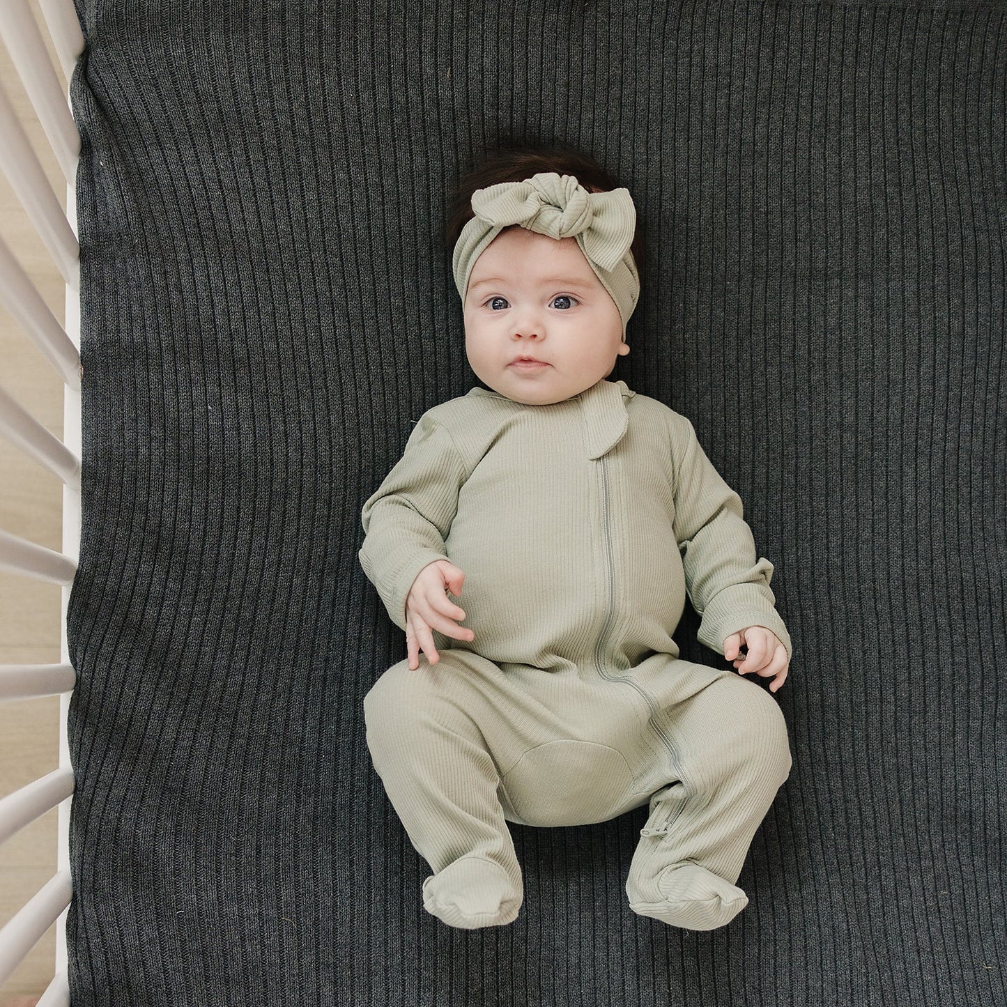 baby girl laying in crib wearing organic cotton zipper pajamas and a matching bow head wrap mebie baby non-toxic eco-friendly