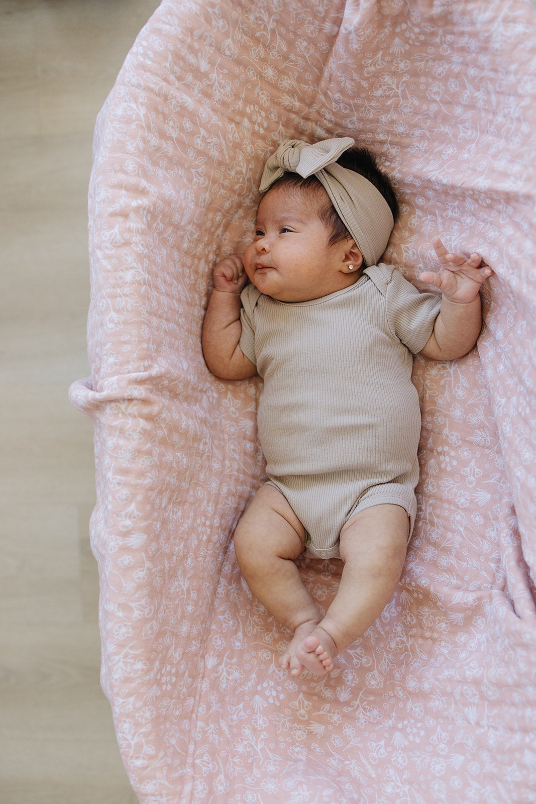 baby in a bassinet wearing organic cotton ribbed beige onesie and a matching bow head wrap mebie baby
