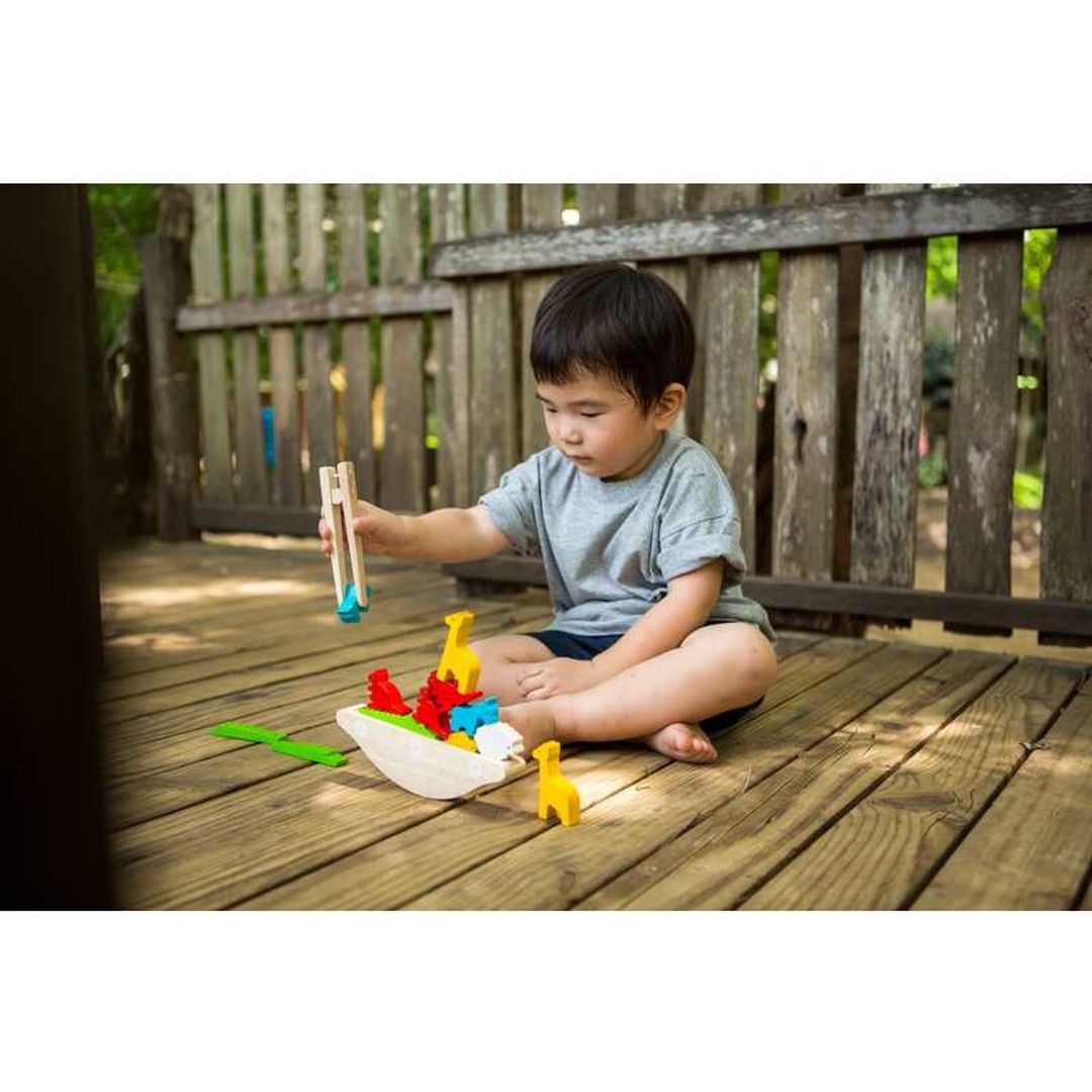 little boy sitting on the deck playing with plantoys wooden eco-friendly balancing boat toy