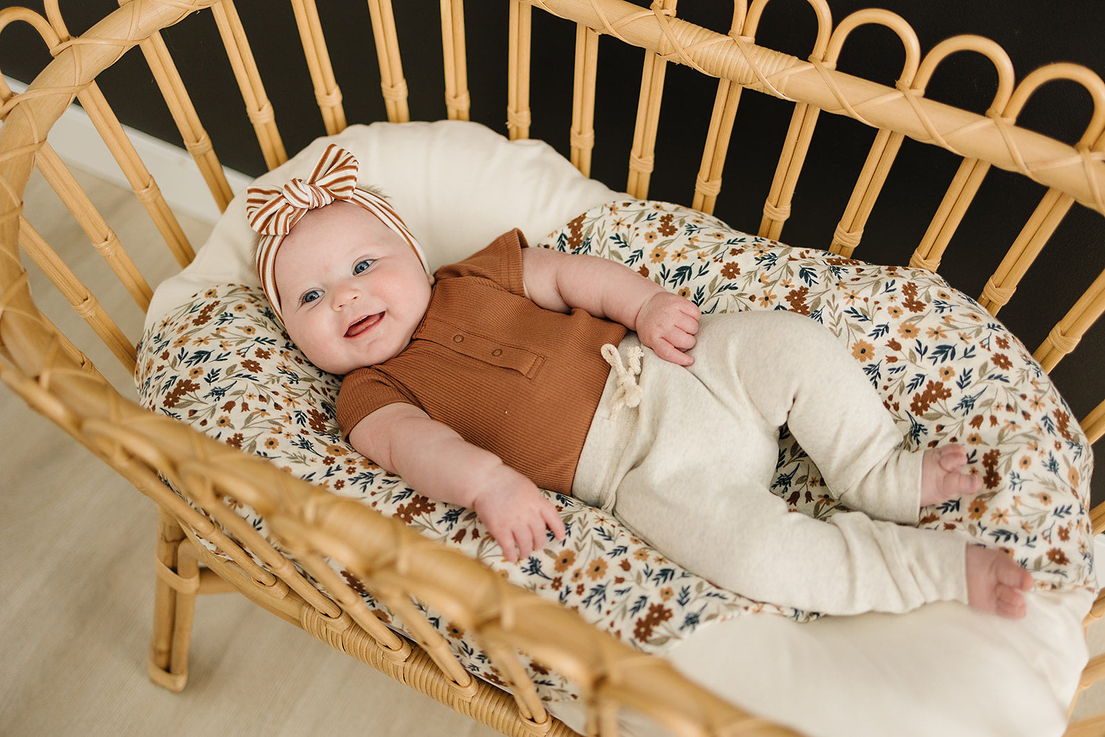 baby girl smiling in bassinet wearing organic cotton rust color onesie and bow head wrap mebie baby