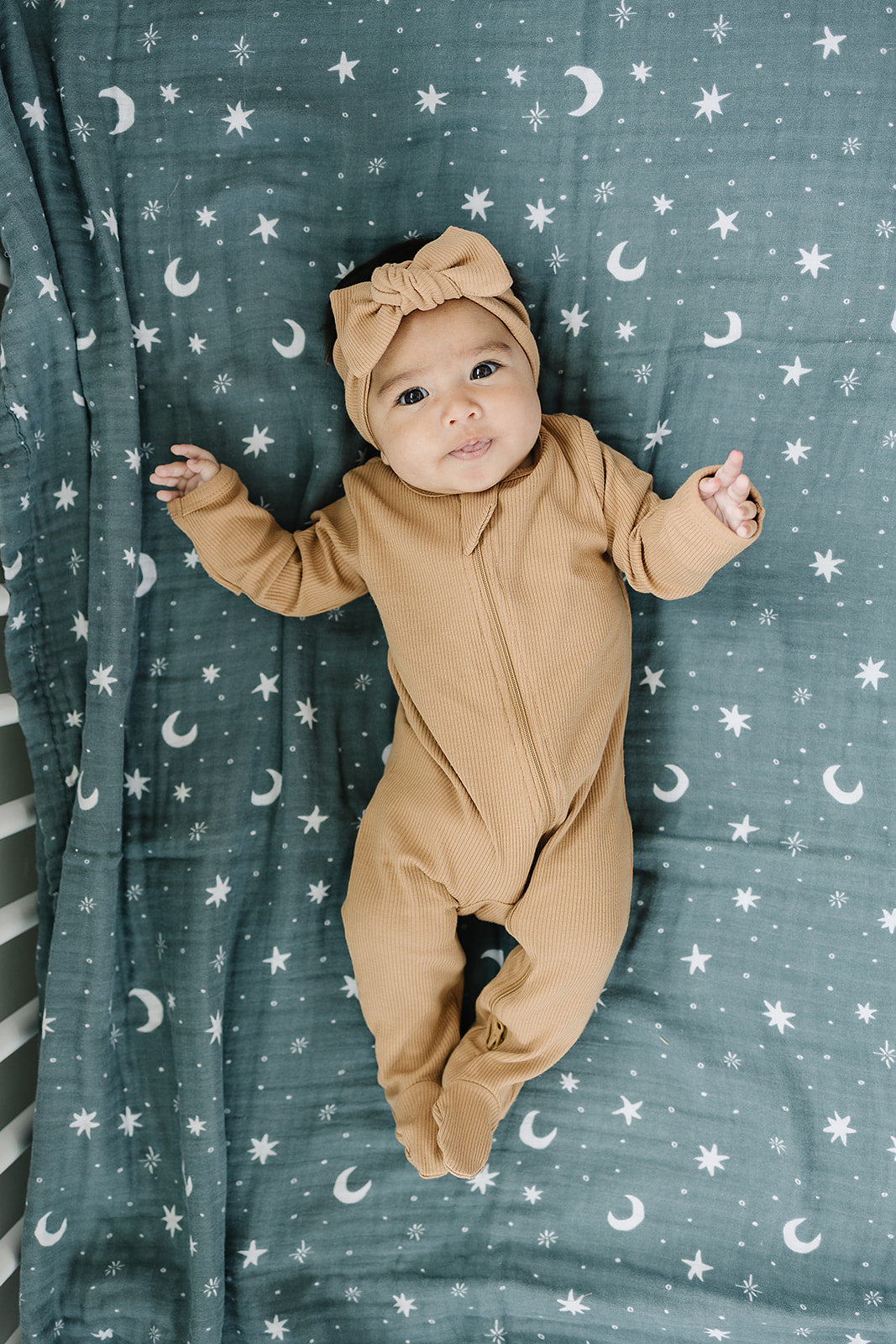 baby girl in a crib wearing organic cotton brown zipper footed pajamas with a matching headband bow