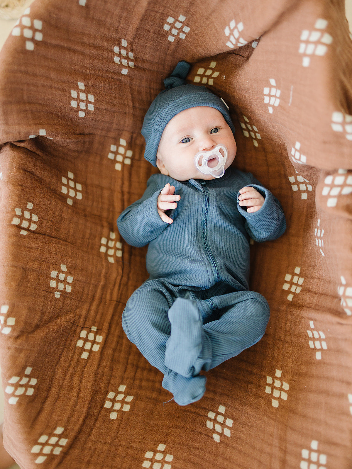 baby laying down with pacifier wearing organic cotton ribbed navy knot hat and matching zipper onesie pajamas by mebie baby