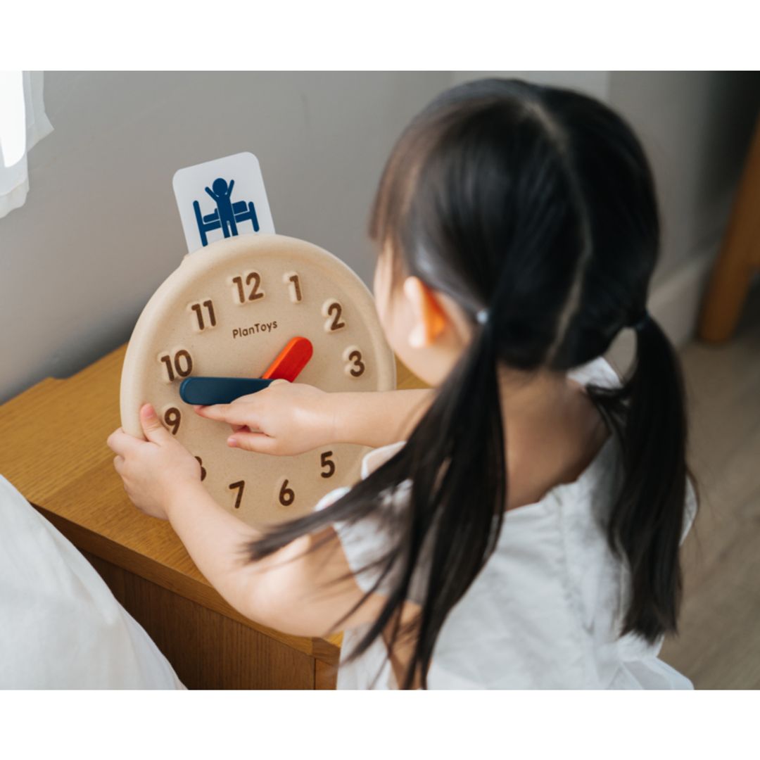 little girl playing with eco-friendly non-toxic wooden clock by plantoys