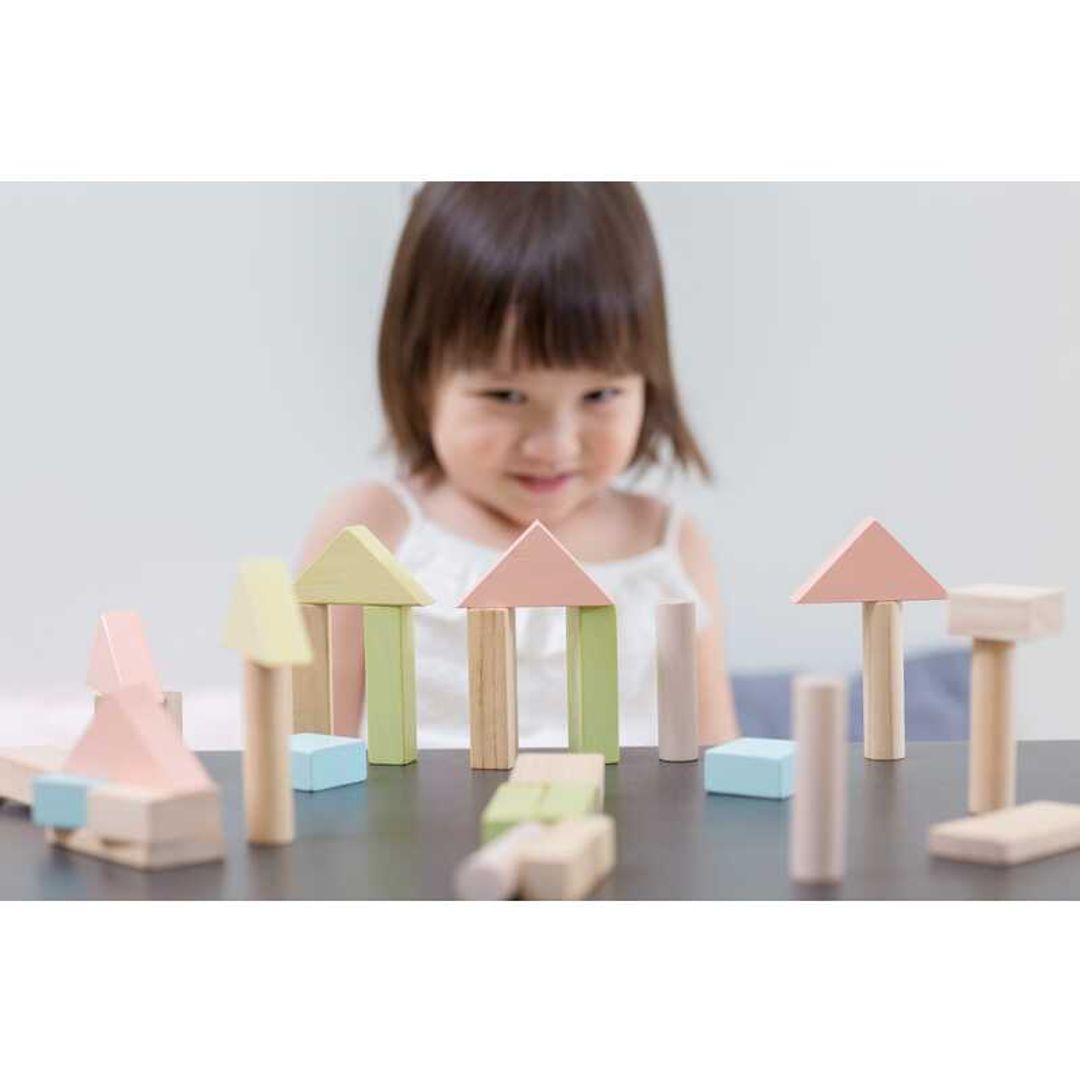 little girl playing with eco-friendly non-toxic wooden building blocks in pastel color by plantoys