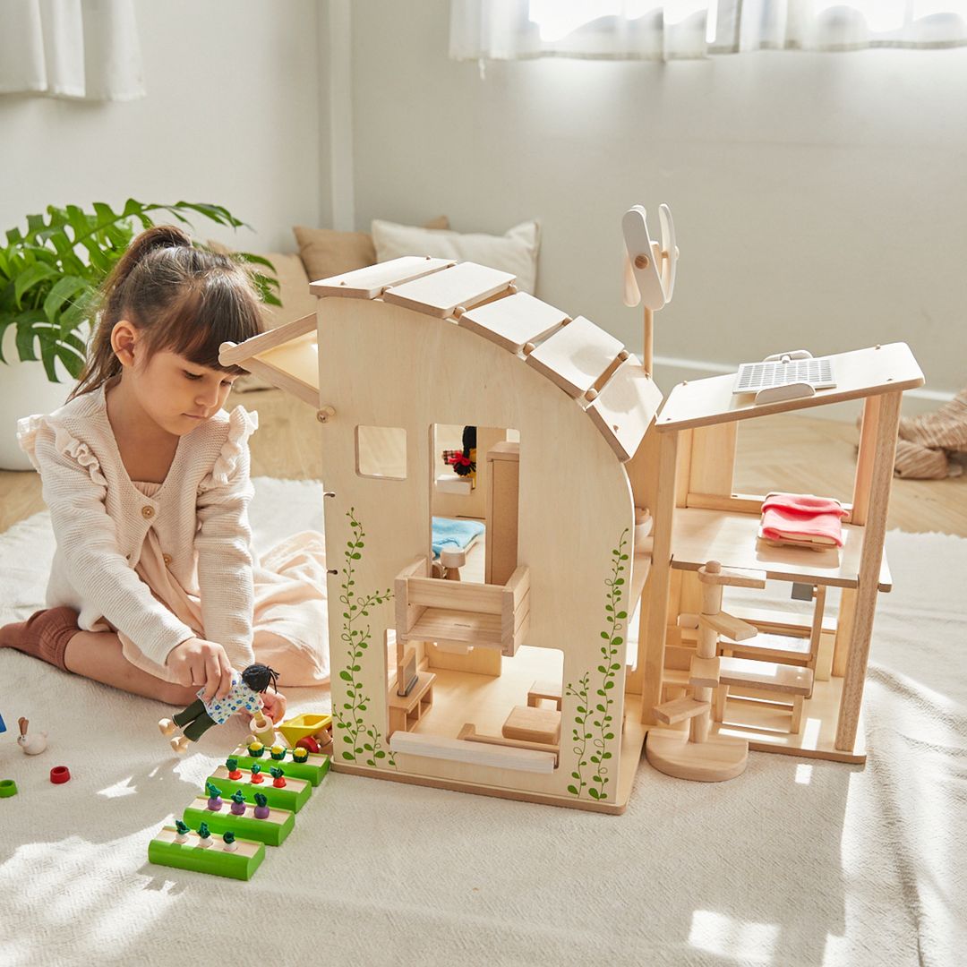 little girl playing with sustainable wooden green dollhouse by plantoys