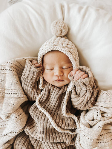 baby sleeping wearing organic cotton knit ribbed beige pullover and leggings and beige bonnet