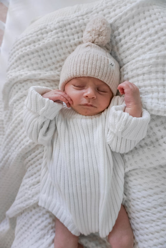 baby sleeping wearing organic cotton ribbed knit onesie sweater and sand color merino wool beanie hat by luna luca