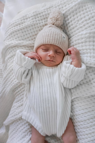 baby sleeping wearing organic cotton ribbed knit onesie sweater and sand color merino wool beanie hat by luna luca