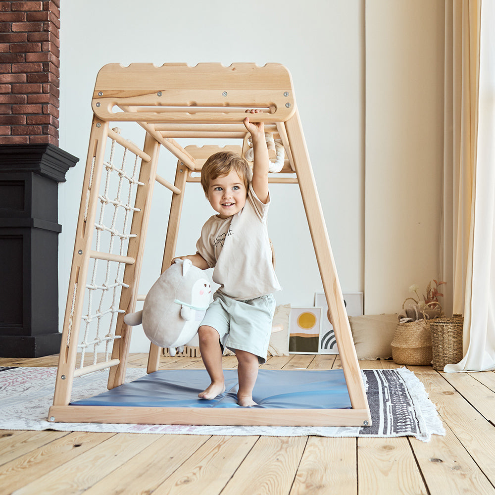 little boy playing with indoor wooden eco-friendly toddler jungle gym playground holding a stuffy 