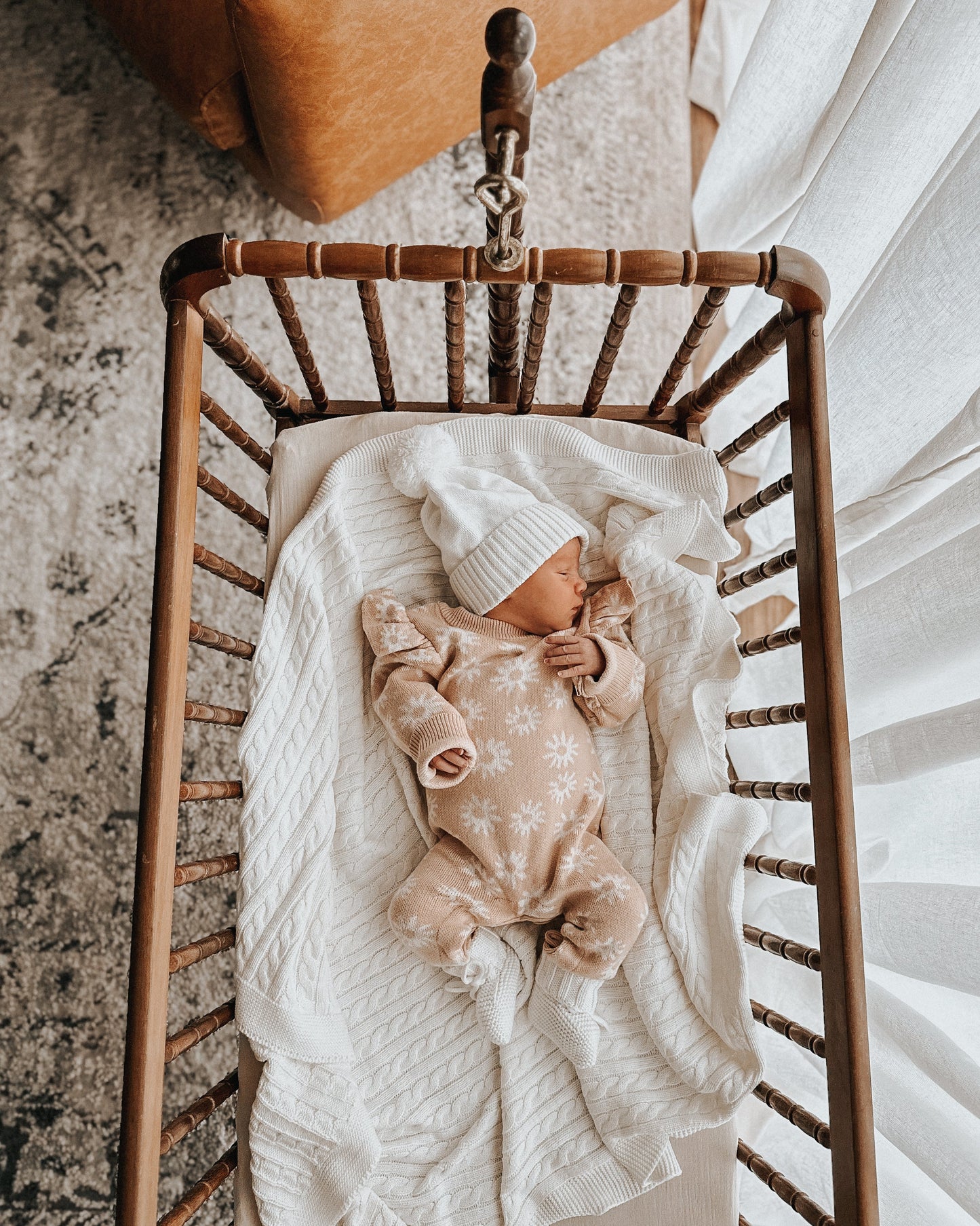 baby sleeping in a crib wearing knit organic romper and knit white beanie hat and matching knit organic cotton booties