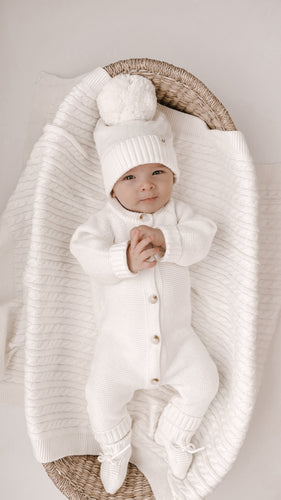 baby in bassinet wearing organic cotton knit jumpsuit with buttons with matching booties and beanie hat