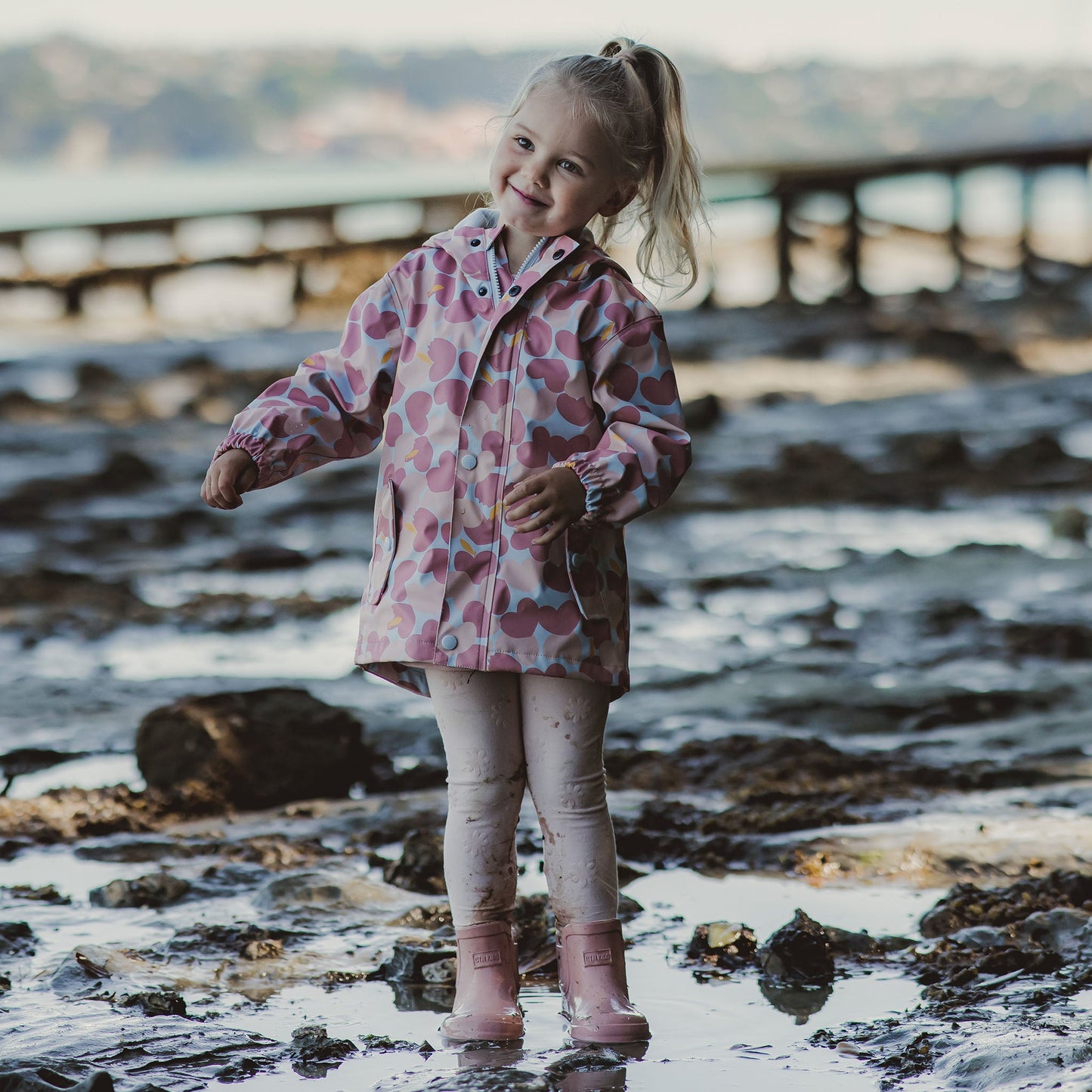 little girl smiling in mud and puddles wearing eco-friendly pink non-toxic rain jacket by snapper rock
