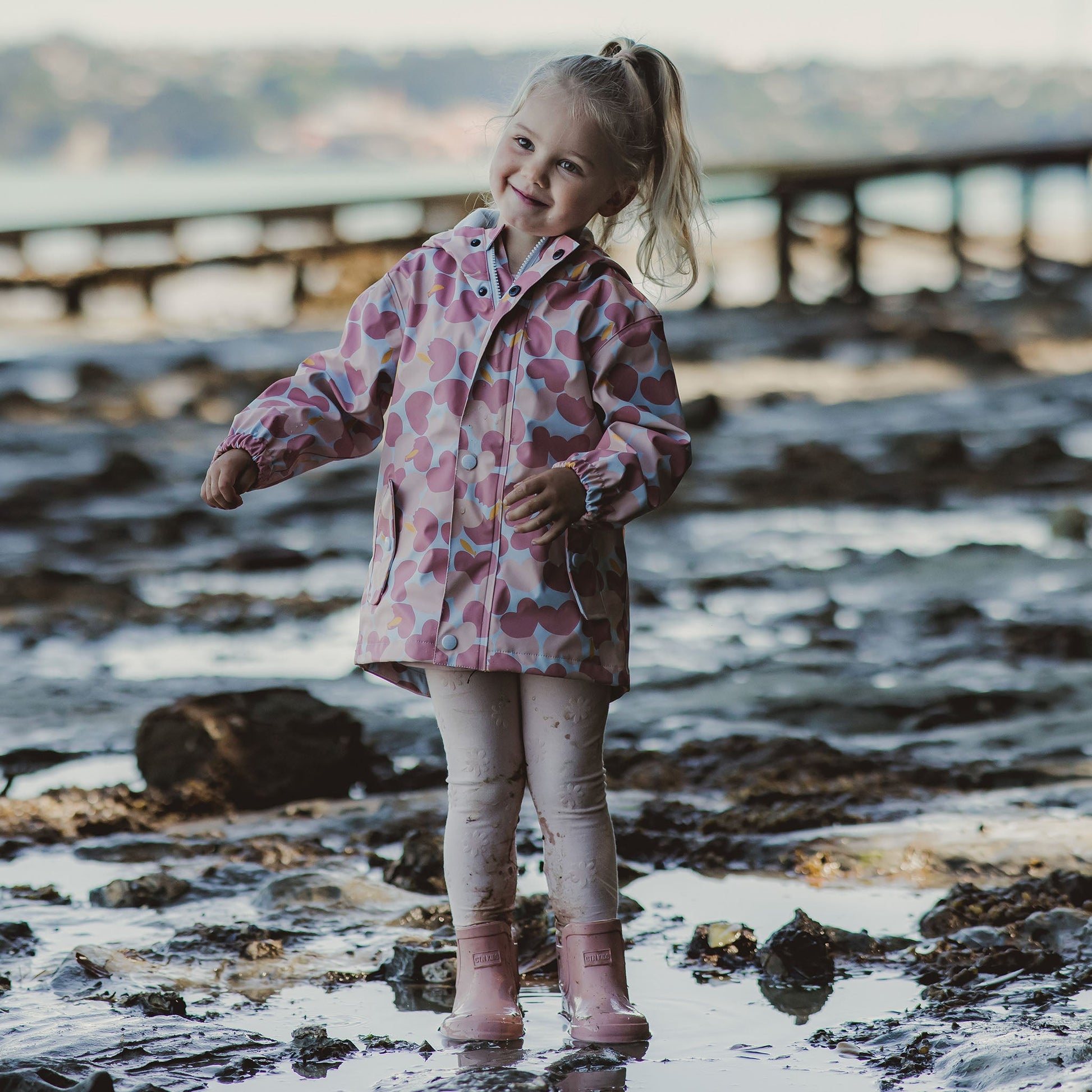 little girl smiling in mud and puddles wearing eco-friendly pink non-toxic rain jacket by snapper rock