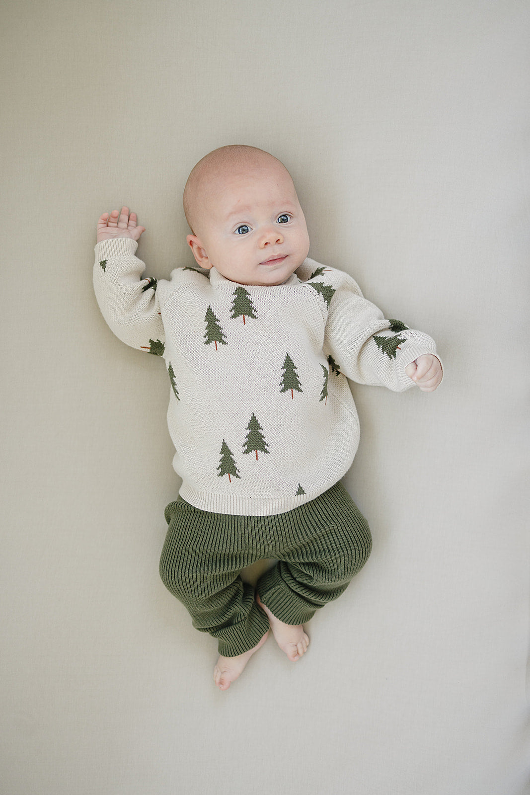 baby laying wearing organic cotton olive knit leggings and a sweater with christmas trees mebie baby