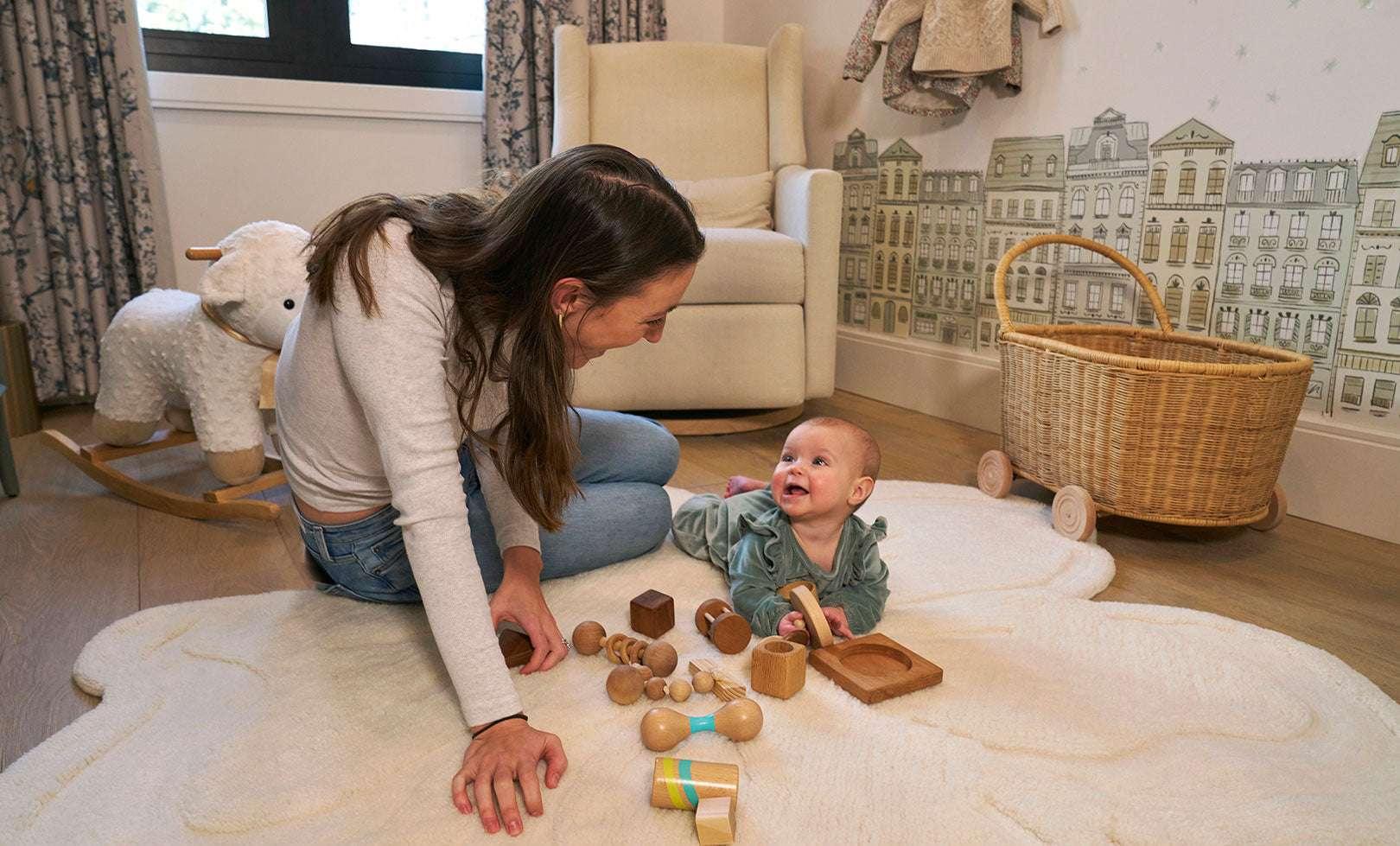 A mother and her baby playing on a beautiful, flower-shaped Sage & Wild wool rug in a minimalist, neutral-toned nursery.
