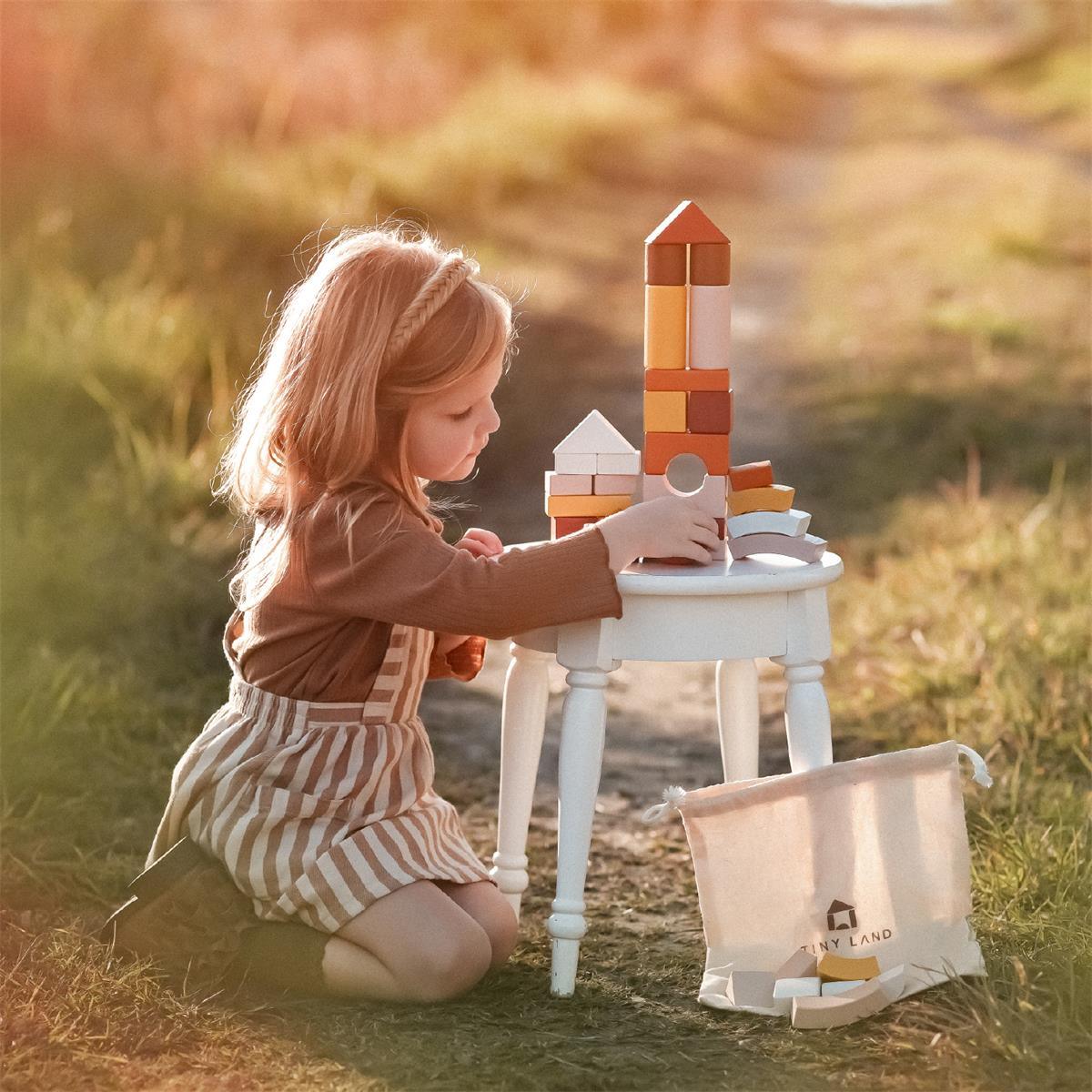 toddler girl playing in nature with eco-friendly wooden blocks by tiny land