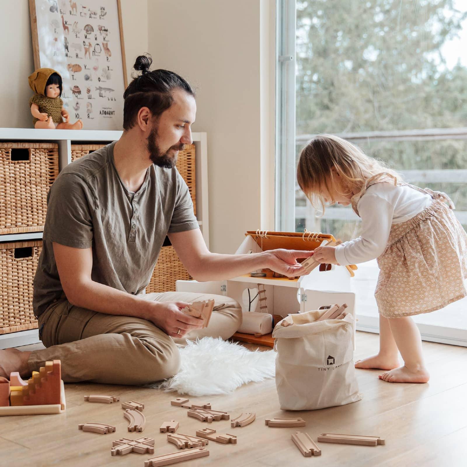 dad and daughter playing with eco-friendly wooden train set on the floor 
