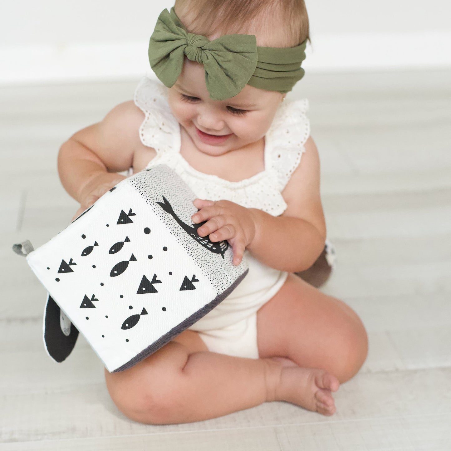 baby girl smiling playing with white and black montessori toy cube by wee gallery